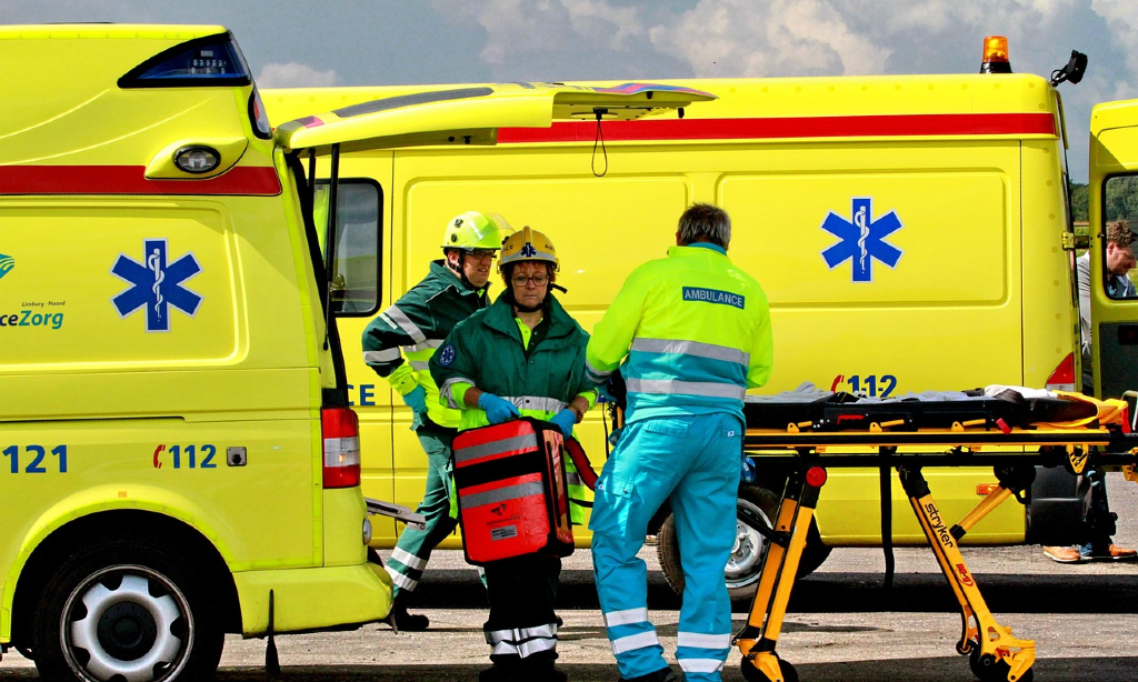 Två ambulanser med personal som står vid en bår utanför.