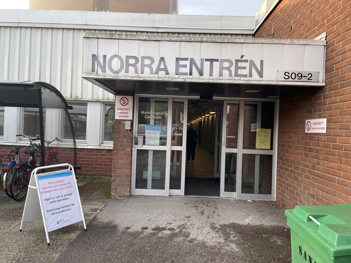 Norra entrén på Sundsvalls sjukhus. Det står Norra entrén med versaler ovanför dörrarna. På marken framför står en gatupratare. Bakom den är det ett takat cykelställ med cyklar.
