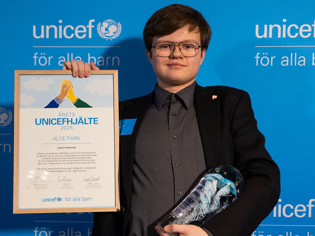 Alve står med sitt diplom och pris framför blå vägg med texten UNICEF
