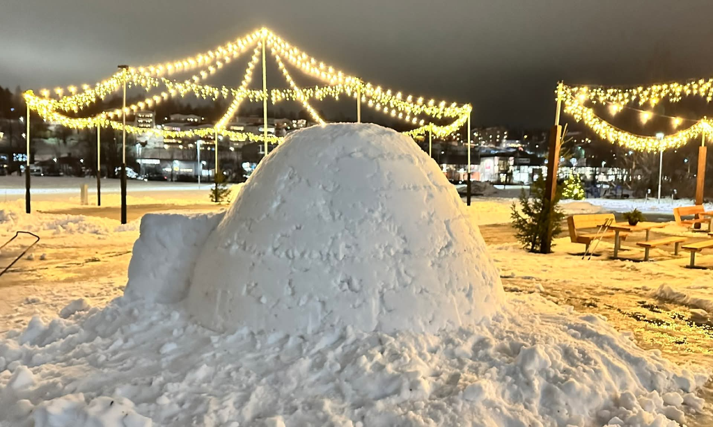 Igloo i närbild. Ljusslingor på paviljonger med bänkar och bord.