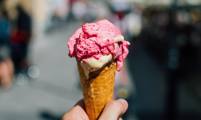 En våffla med två glasskulor som smälter lite. Den övre är rosa. Bara tumme och pekfinger syns av handen.