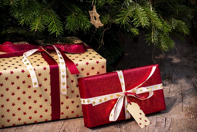 Två inslagna julklappar under en gran. Ett med vitt papper och röda stjärnor och ett med rött papper med stjärnor. De har röda och vita snören.