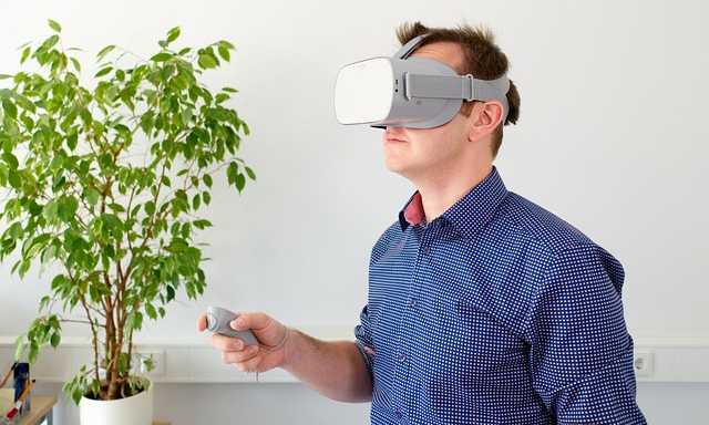 Man med VR-glasögon som håller i en manöverdosa. En benjaminfikus i vit kruka i ett hörn i bakgtunden