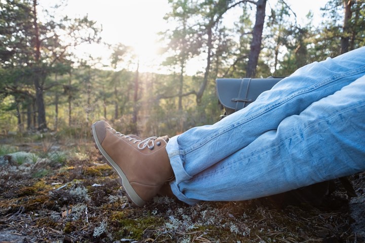 Någon sitte rpå en höjd i skogen. Endast jeansklädda ben och bruna kängor syns.