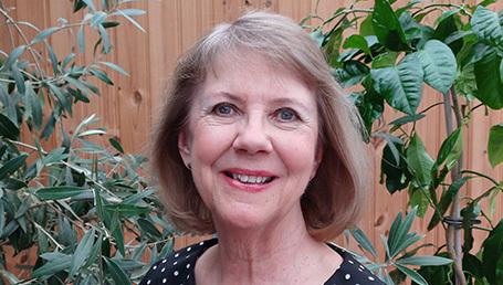 En glad Eva Ullerud framför gröna växter. Hon har ljusbrunt hår nästan ner till axlarna.