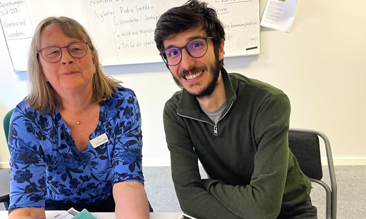 Murat och läraren Lena sitter framför en whiteboard , och bakom ett bord.