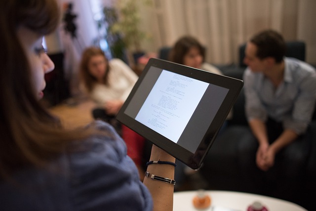 En tjej läser på sin Ipad. I bakgrunden sitter några ungdomar och pratar.