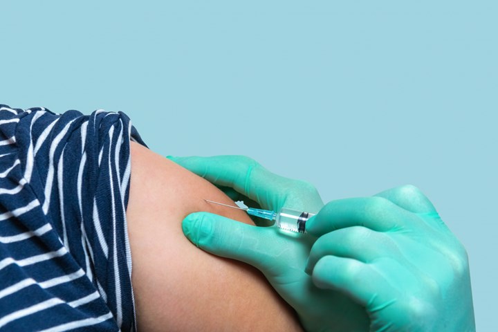 Axel med upprullad ärm. Händer i gröna handskar ger vaccin högt upp på axeln..