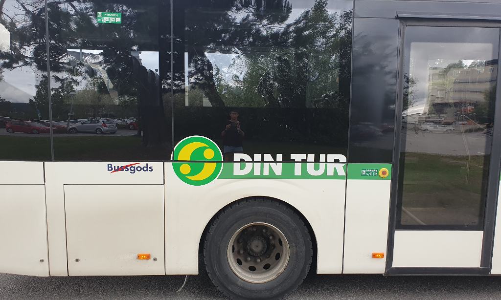 närbild på ena v Din Turs bussar. Den är vit med grön rand. Din tur i vit text. Loggan som är rund med grön botten. Två gula böjda streck med punkter.