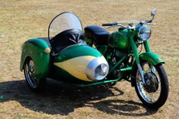 En grön motorcykel med sidovagn stående utomhus. Gräset är lite brunt.