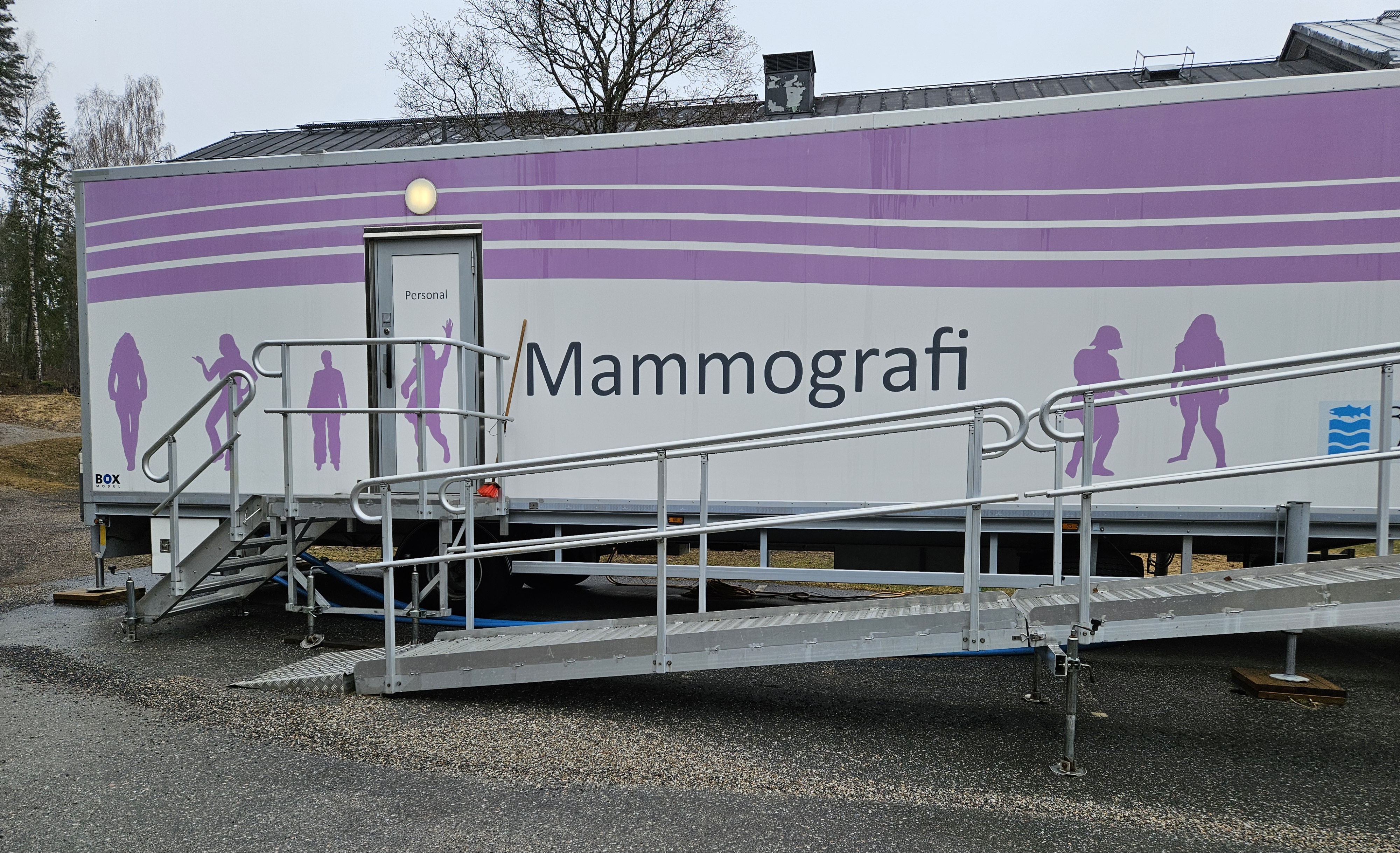 En av Region Västernorrlands vita mammografivagnar med lila vågor överst. Dets tår Mammografi i svart och lila människor. En lång ramp i metall upp till ingången