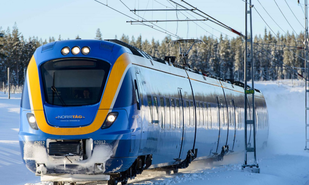Vinterbild med Norrtåg på spåret. Elledningar bredvid spåret.