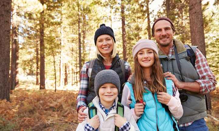 En glad familj på fyra personer i skogen. Solstrålar skiner genom skogen i bakgrunden.