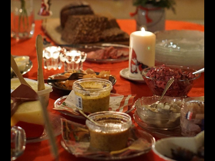 Del av julbord med sillar, rödbetssallad, ost, skinka och bröd. Julljus mitt på bordet.