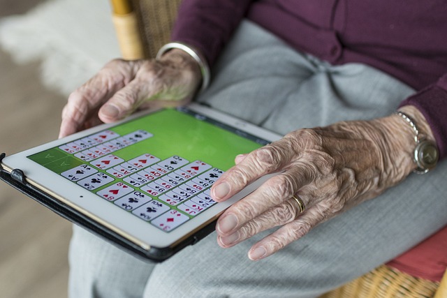 En äldre persons händer håller en surfplatta i knät. Personen spelar patiens.