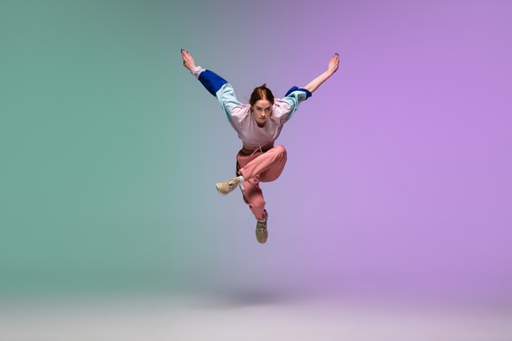 En dansare som hoppar upp från golvet. Bakgrunden går i lila och grönt.