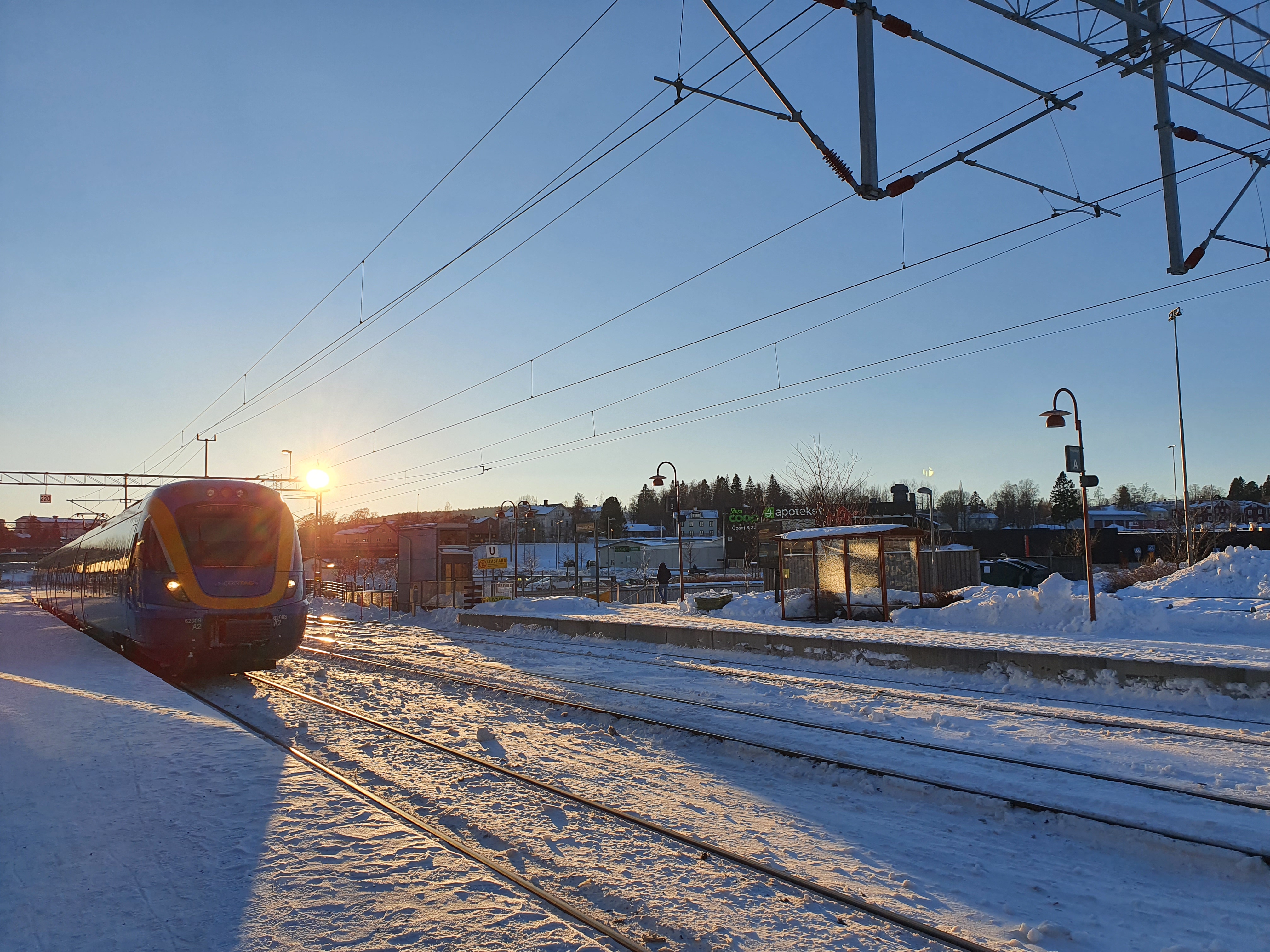 Norrtåg närmar sig perrongen en vinterdag. Solen på väg upp.