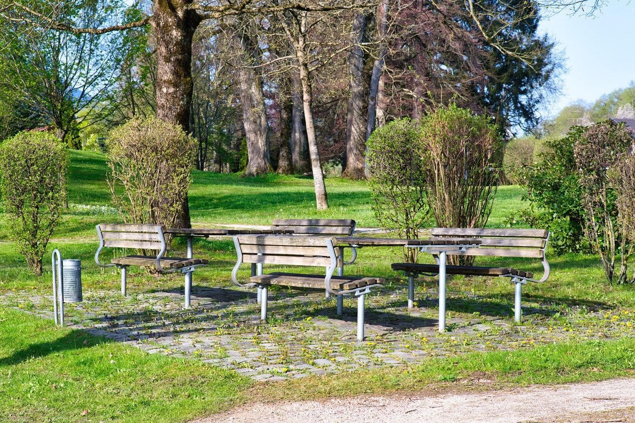 Bord och bänkar i ett grönområde. Träd och buskar runtom.En gångväg alldeles intill.