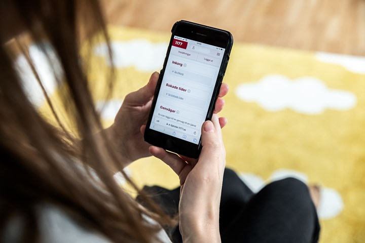 En person sitter och loggar in på 1177.se på sin mobil. De tär händerna och mobilskärm som syns.