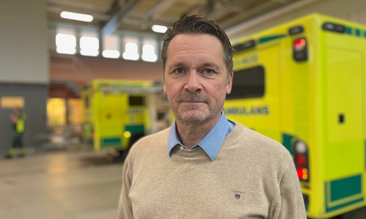 Peter Neumann och ambulanser i bakgrunden inne i en ambulansstation. Ambulanserna är gula med gröna fält