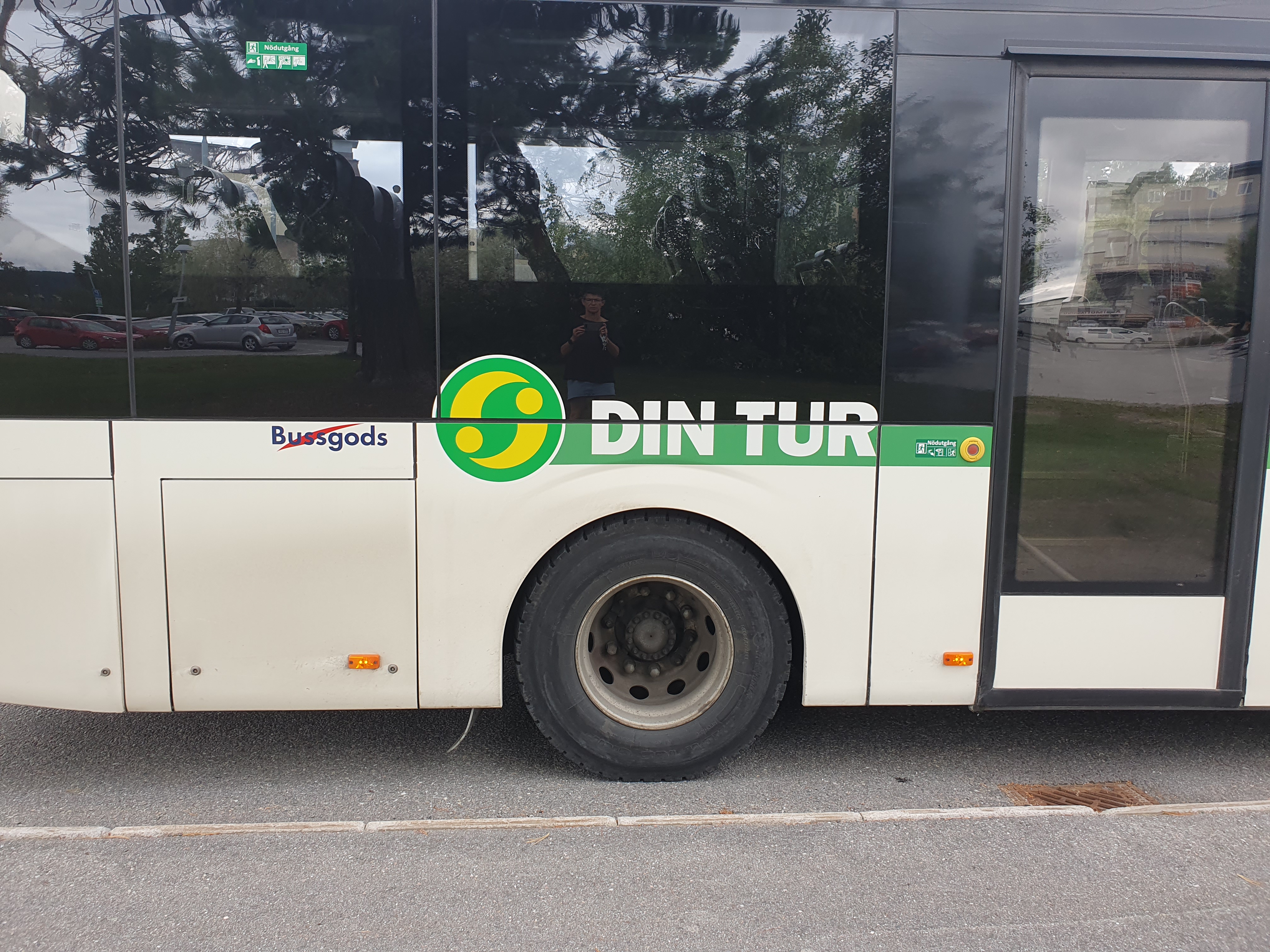 Bakre delen på en vit buss. Det står Din tur och dess symbol på sidan. Bakre dörren till höger i bild.