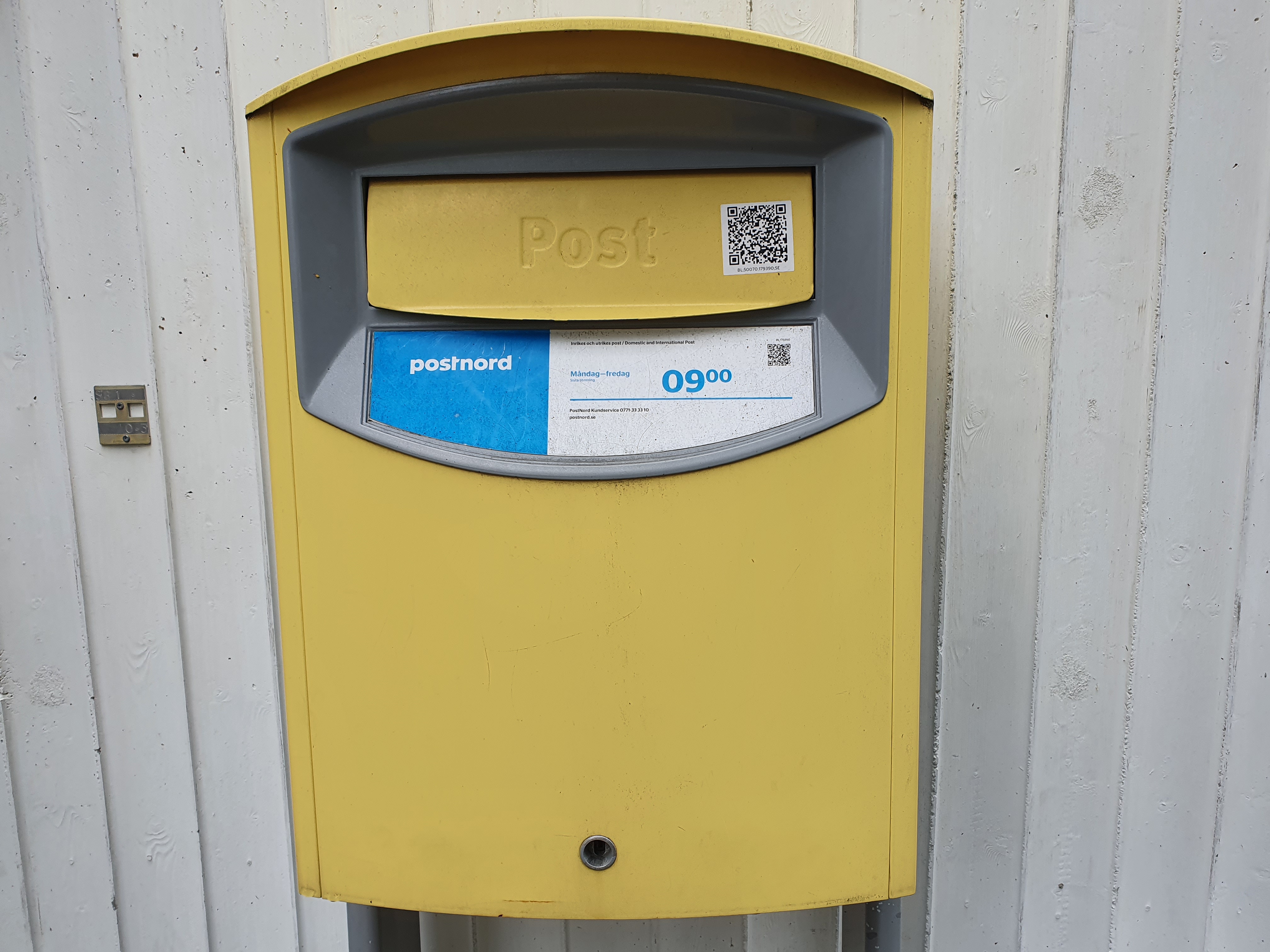 Postnords gula postlåda på en vägg.