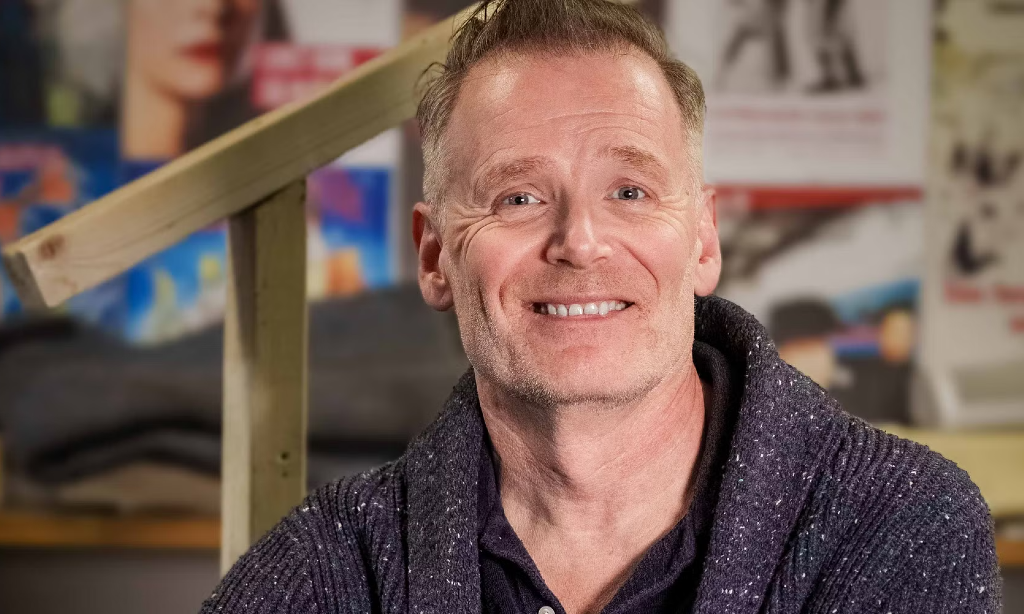 En glad Patrik Pettersson sittande med trappräcke på sin högrasida. Han har en mörkblå kofta.