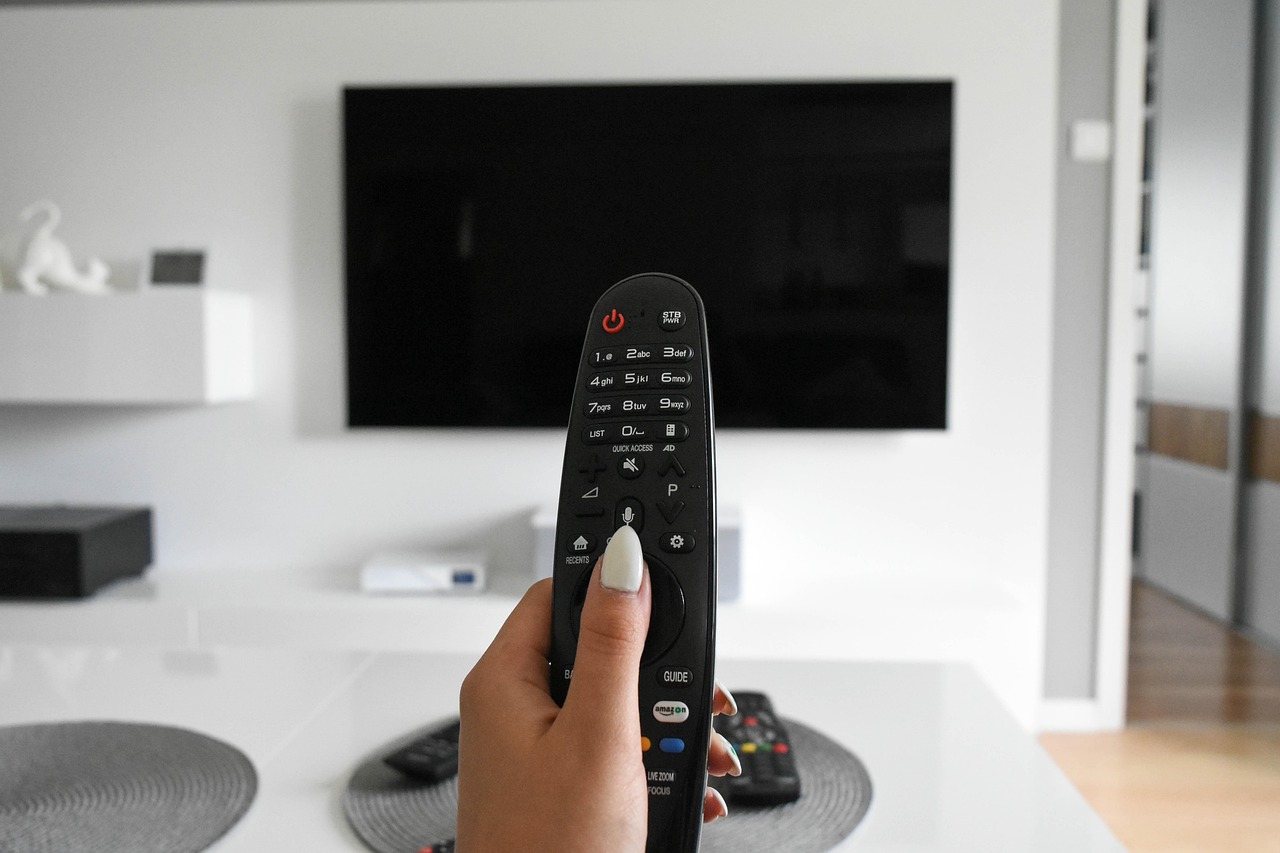 Hand med tv-dosa riktad mot tv-skärm på vägg.