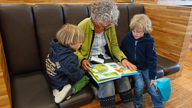 Äldre kvinna sitter på en svart skinnsoffa och läser ur en bok. Ett barn på var sida