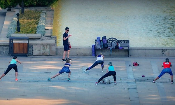 personer som gör gymnastikövningar utomhus. Yogamattor ligger på en bänk framför..
