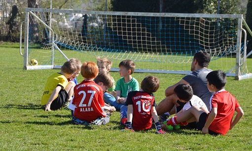 Barn sitter framför fotbollsmålet på fotbollsplan med en tränare.