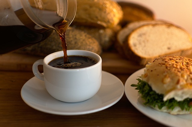 Kaffe hälls upp och en fralla på assiett bredvid. Bröd i bakgrunden.