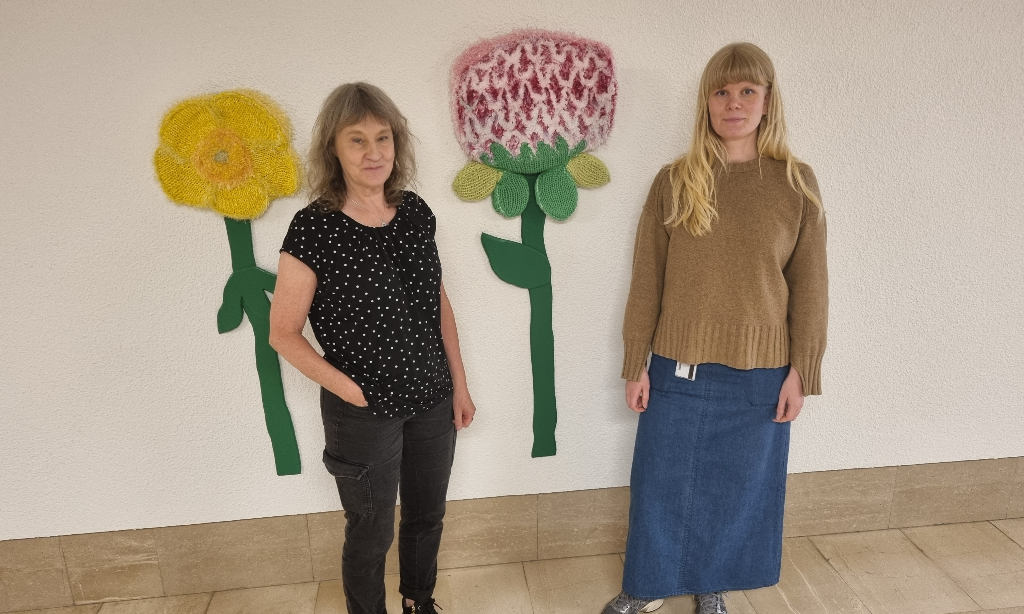Konsthandläggarna Eva-leena och Lovisa på konststråket Gatan. de står framför taktil konst som föreställer två stora blommor.