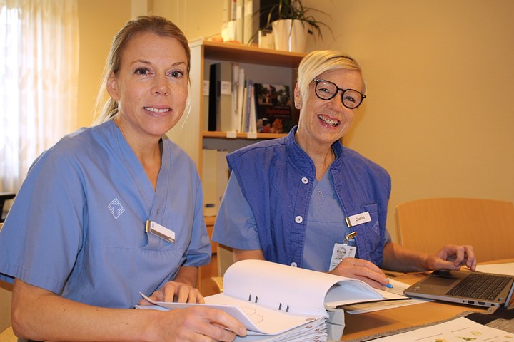 Dietisterna Anna och Camilla sitter bakom ett skrivbord. De har sina blå arbetskläder.